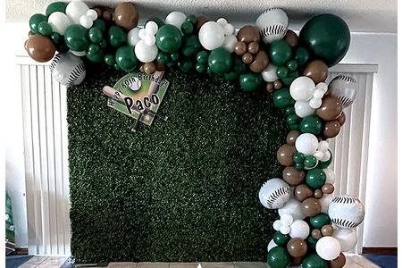 Baseball themed Organic balloon garland with foil baseball, greenery backdrop and custom sign. The colors are green, brown and white.