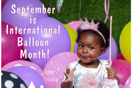 September is International Balloon Month. The picture features a sweet baby girl in a princess costume in amongst a bunch of pinks and purple balloons.