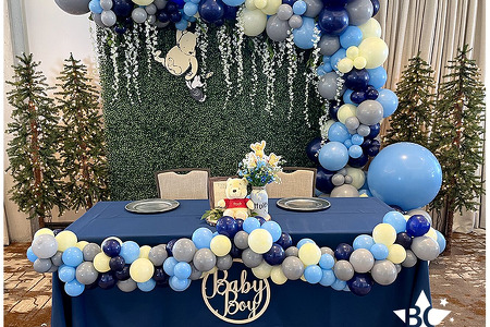 Baby Boy Winnie the Pooh Baby Shower. Light blue, yellow, grey and Navy organic style balloon garlands with greenery backdrop, white flower vines, winnie the pooh holding piglet cutout. Balloons Hotel  Melby Melbourne FL