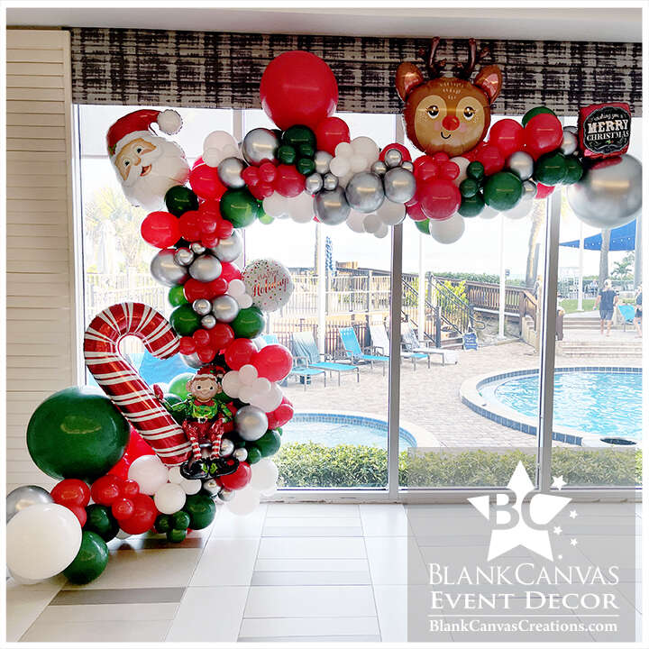 Organic Style Balloon Garland used as a backdrop for photos. It features red, green white and silver balloons with candy canes, elf, santa and rudolph foil balloons.