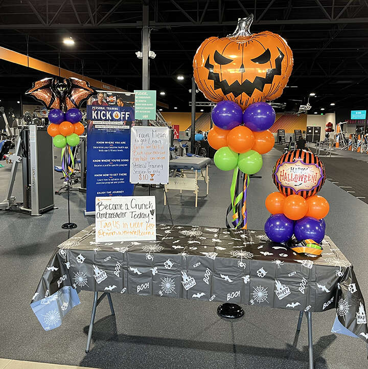 Halloween themed balloon party pole with a jack-o-lantern on top. the colors are orange, purple, lime green and black.