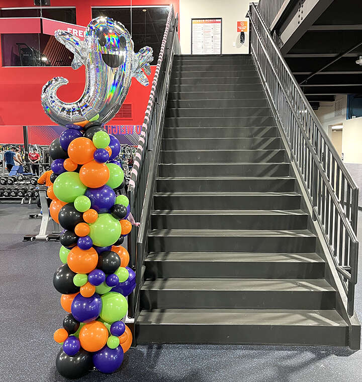 Halloween themed organic balloon column with a ghost on top. the colors are orange, purple, lime green and black.