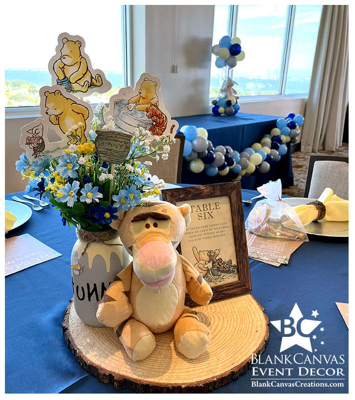 Winnie the Pooh centerpeice on wood plank with table number and wild flowers in a honey pot jar.